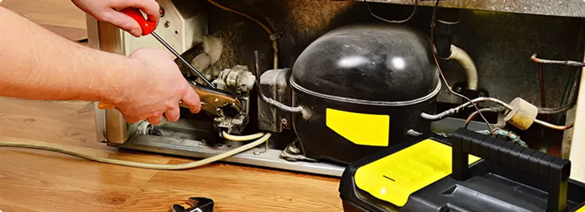 Refrigerator repair technician fixing the compressor and wiring in Hollis, NH
