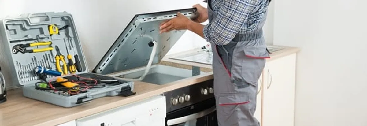 Cooktop repair technician lifting a built-in stovetop for service in Nashua, NH