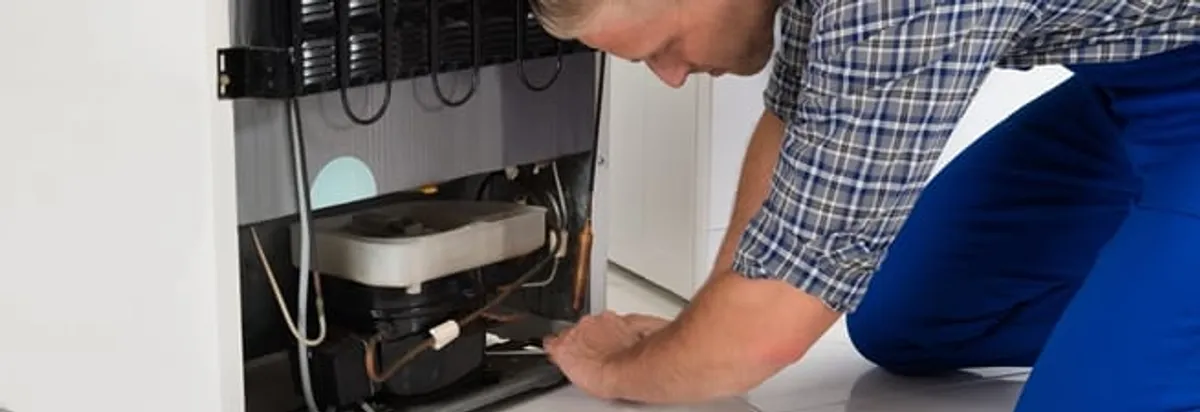 Refrigerator repair technician servicing the compressor and condenser area in Nashua, NH